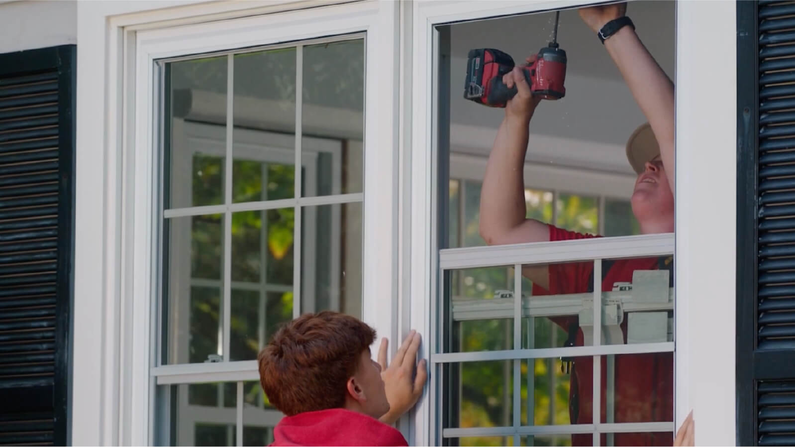 Man on ladder drilling in window frame