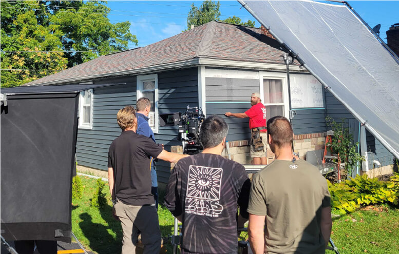 Behind the scenes filming of man adding siding to house with Comfort t-shirt on